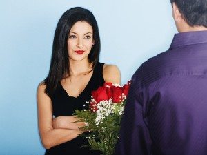 Young man giving skeptical girlfriend flowers