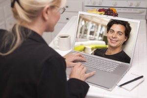 Happy Young Woman In Kitchen Using Laptop Online Dating Search with Portrait of Man On Screen.