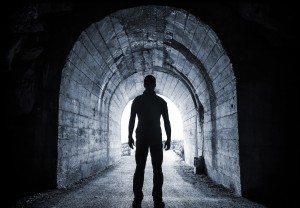 Man stands in dark tunnel and looks in glowing end