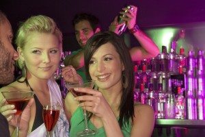 Two young women holding martini glasses at a bar counter