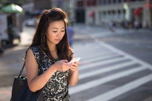Young Asian Woman texting on cellphone on city street