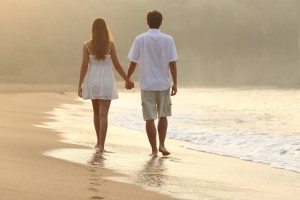 Couple walking and holding hands on the sand of a beach