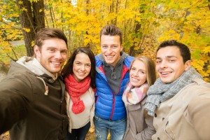 group of smiling men and women in autumn park