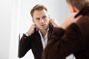 Stylish confident young man looking at himself in mirror