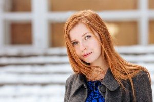 Closeup portrait of young beautiful redhead woman in blue dress and grey coat at winter outdoors