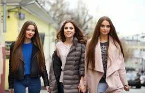 Three young beautiful girlfriends in autumn clothes walking on t