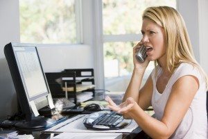 Woman in home office with computer using telephone frowning