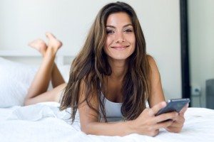 Beautiful young woman using her mobile phone in the bed.